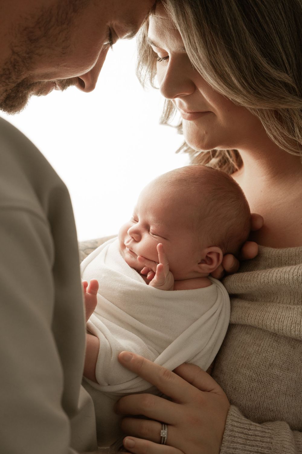 A tender moment between parent and newborn baby in soft natural light against a cream colored background.