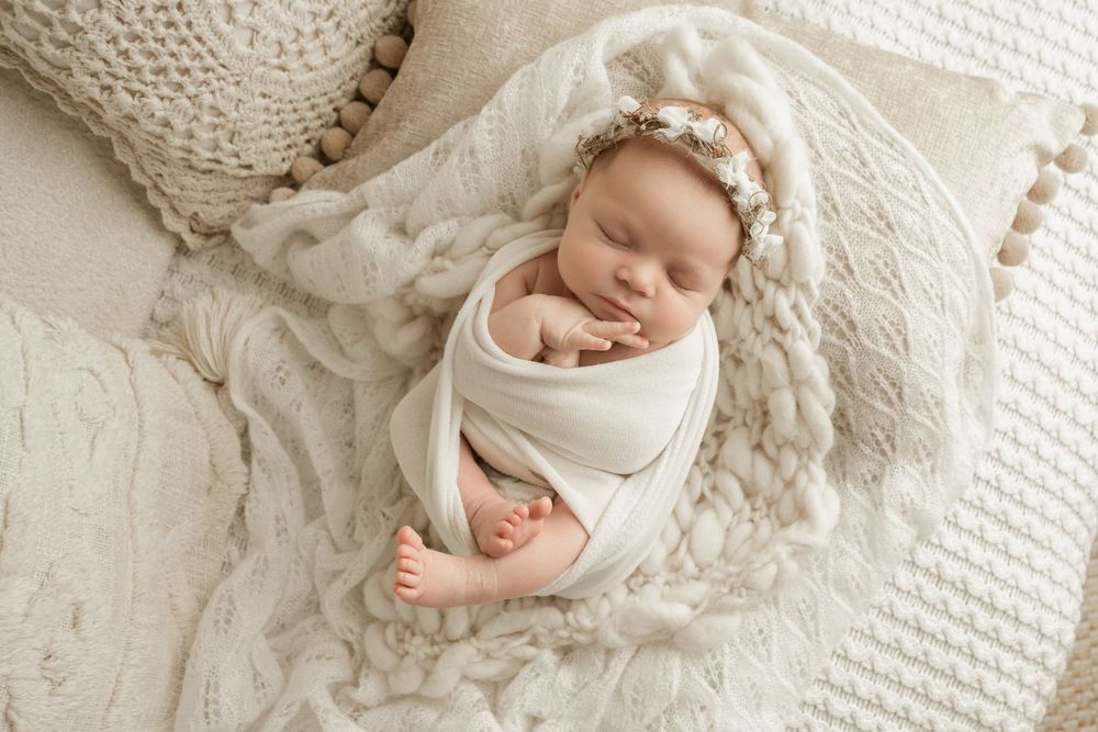Newborn baby sleeping peacefully on white textured blanket during professional photography session.