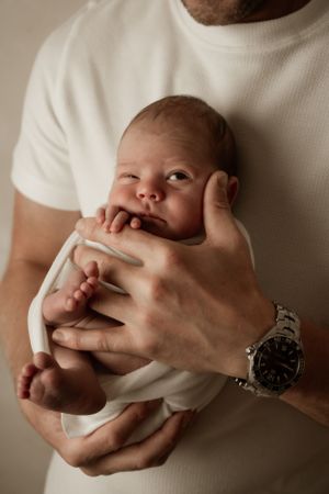 A newborn infant being gently cradled in the arms of someone wearing a white shirt and watch.