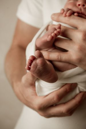 Close-up of tiny newborn baby feet being held in gentle adult hands against white fabric.