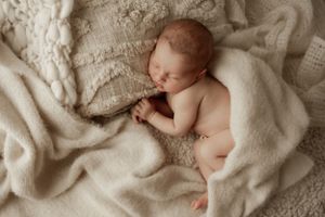 Peaceful sleeping newborn on textured cream blanket during professional photo session.