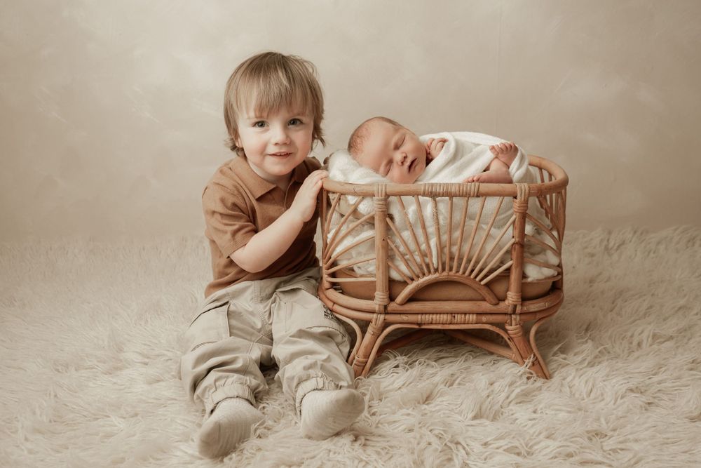 Two siblings posing for a portrait with the baby sleeping in a wicker bassinet.