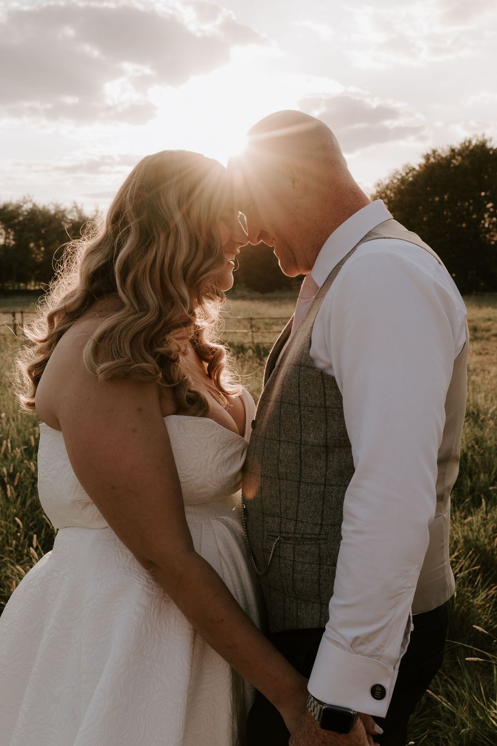 Romantic sunset wedding photo of a couple in a field with golden light streaming through their embrace.