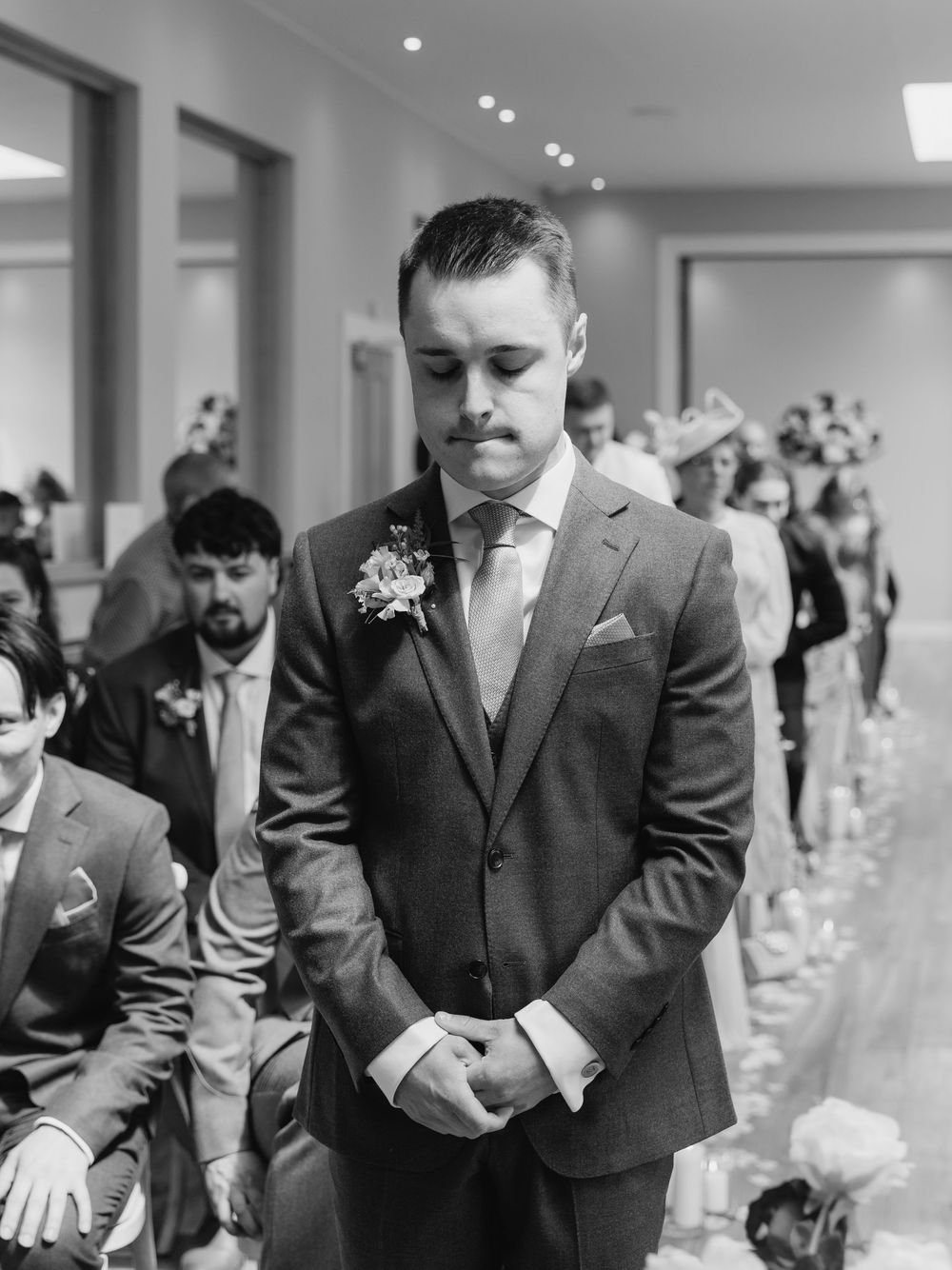 Black and white photo of a formal wedding ceremony capturing an emotional moment with a groom standing at the altar.