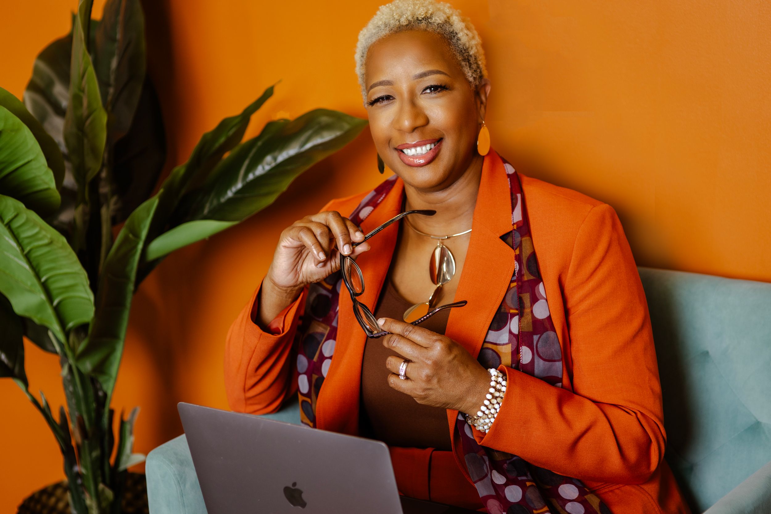 Creative business portrait with orange blazer against warm-toned background with decorative plants.