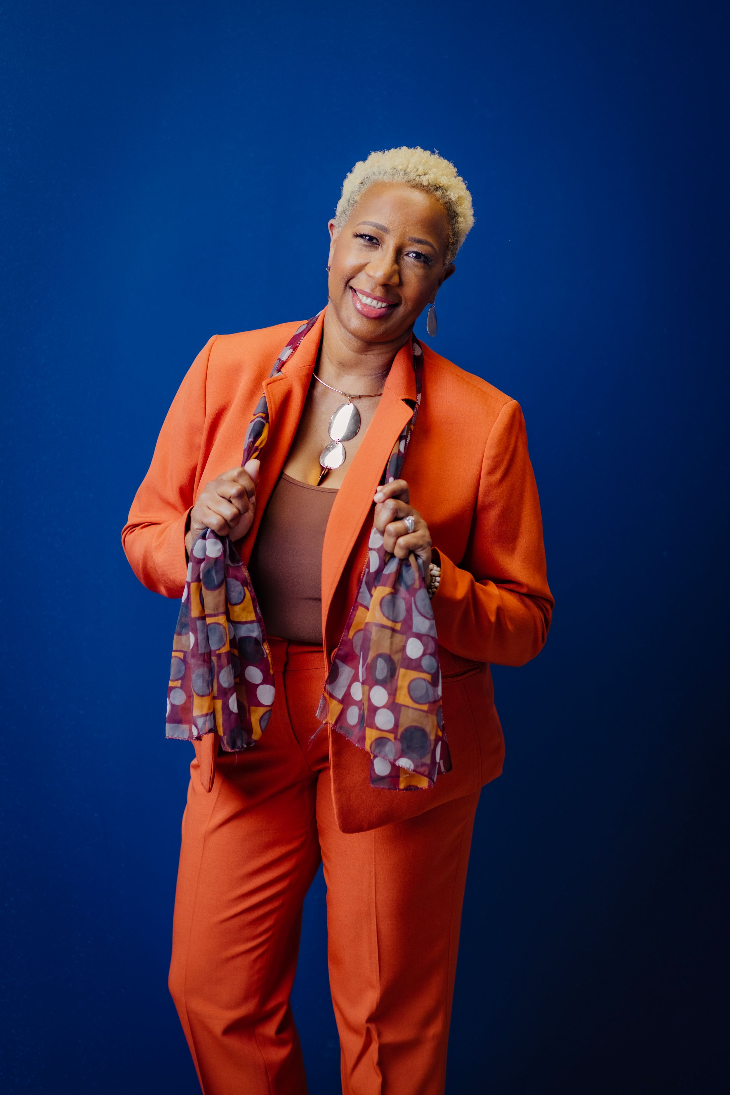 Vibrant orange suit ensemble photographed against deep blue studio background.