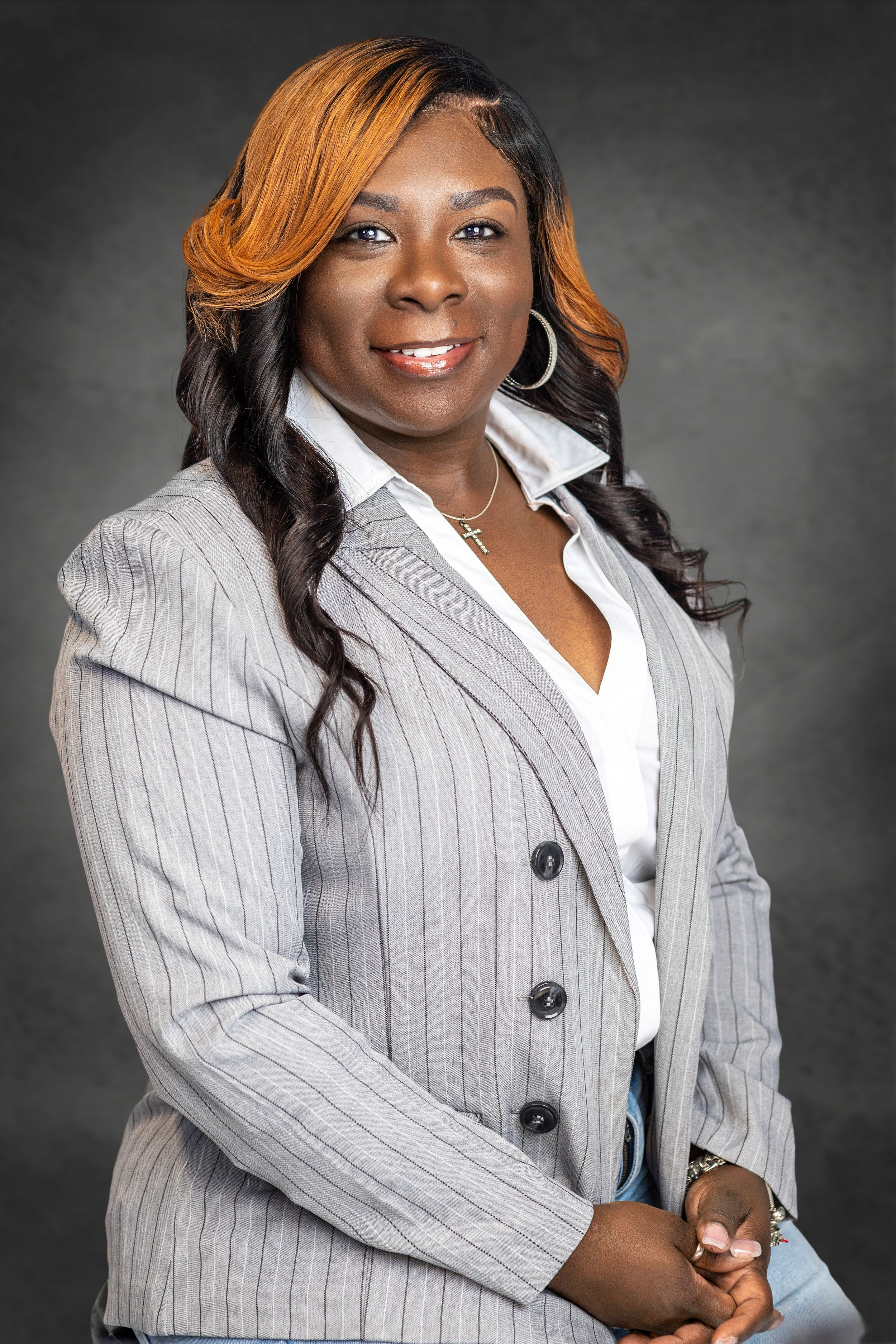 Professional portrait in pinstriped grey blazer against dark backdrop.