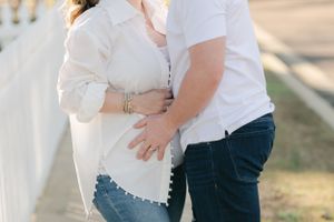 Close-up of pregnant couple embracing, hands resting on baby bump, wearing jeans outdoors.