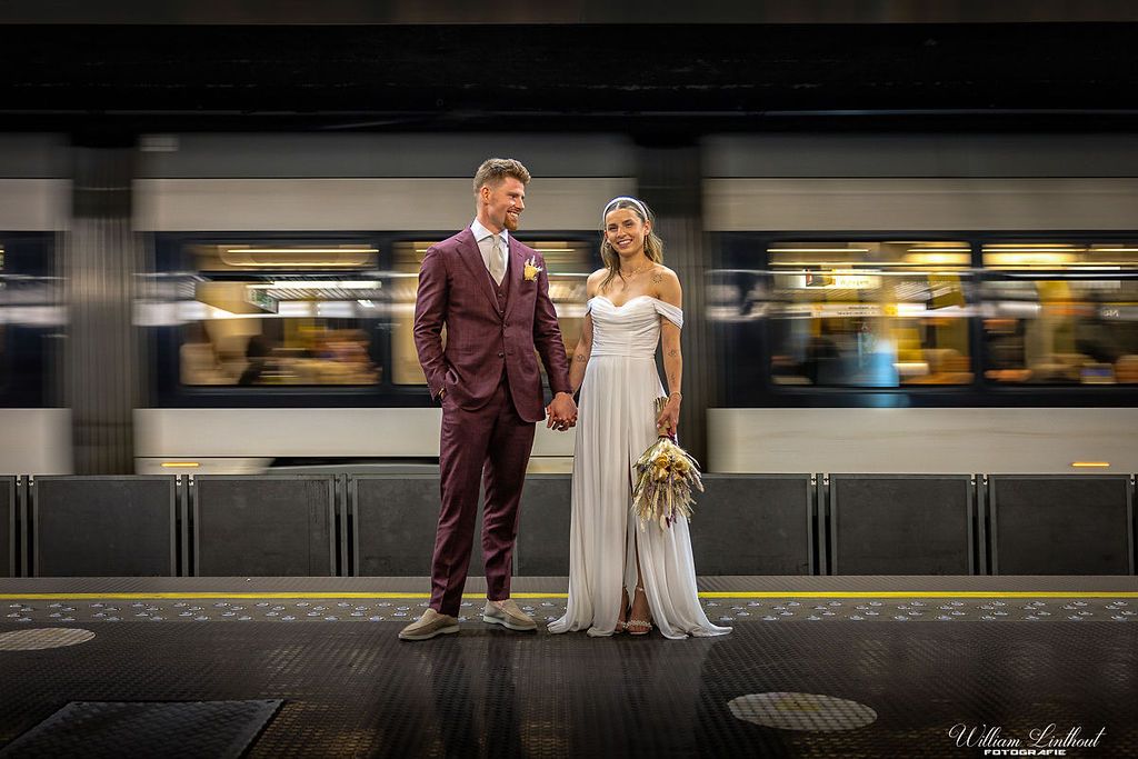 A couple poses on a subway platform in formal wedding attire.