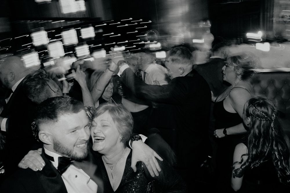 Black and white photo capturing joyful dancing and laughter at a formal event.