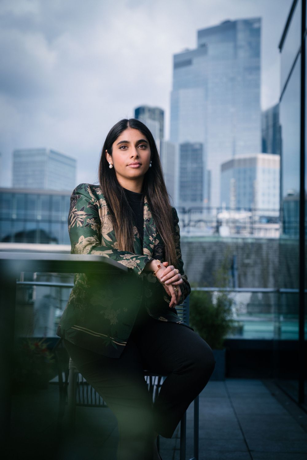 Professional portrait against modern city skyline featuring fashionable camo jacket and dark outfit.