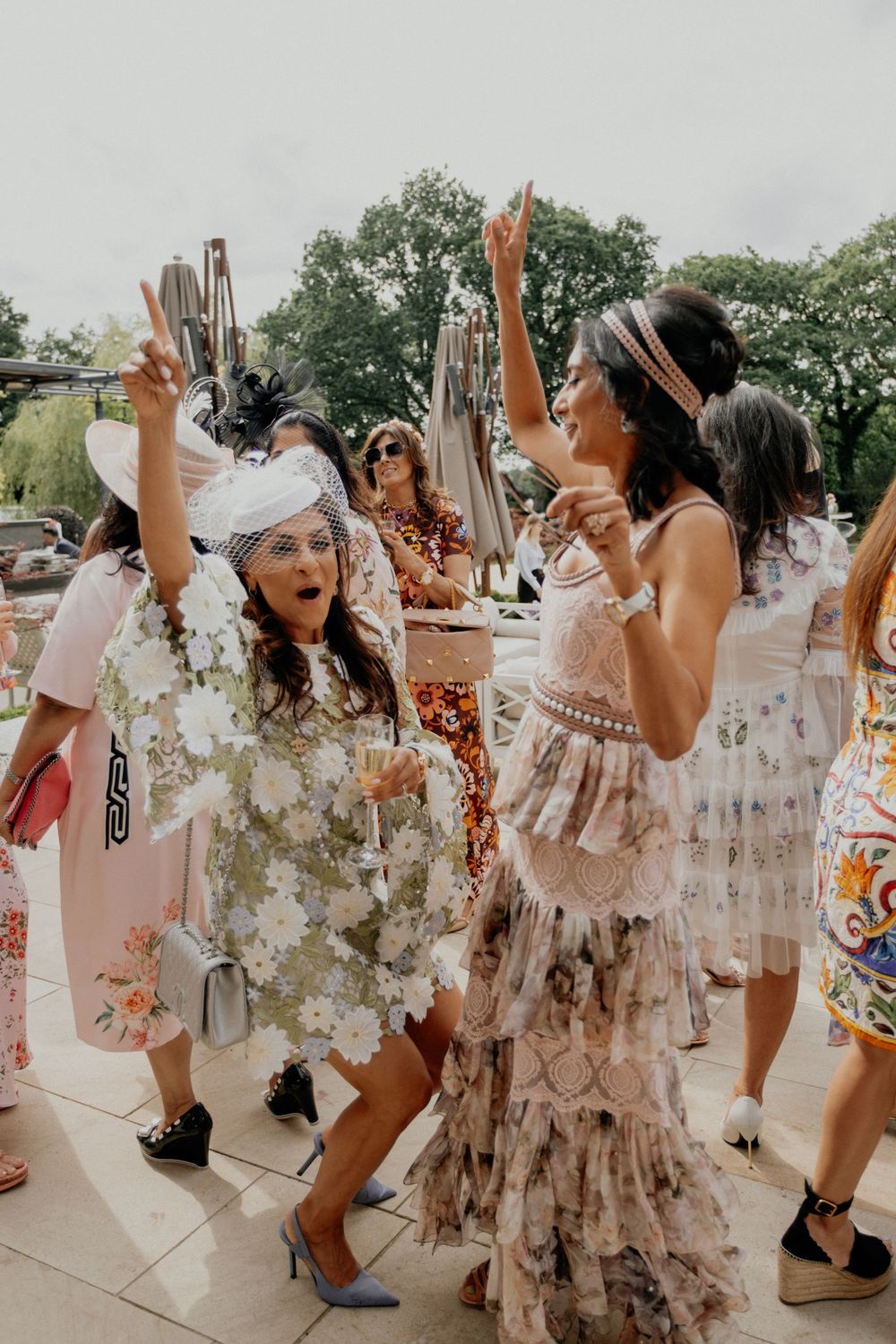Wedding guests in floral dresses dancing and celebrating outdoors.
