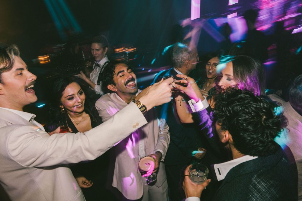 Energetic nightclub scene with party-goers dancing and celebrating under purple lights.