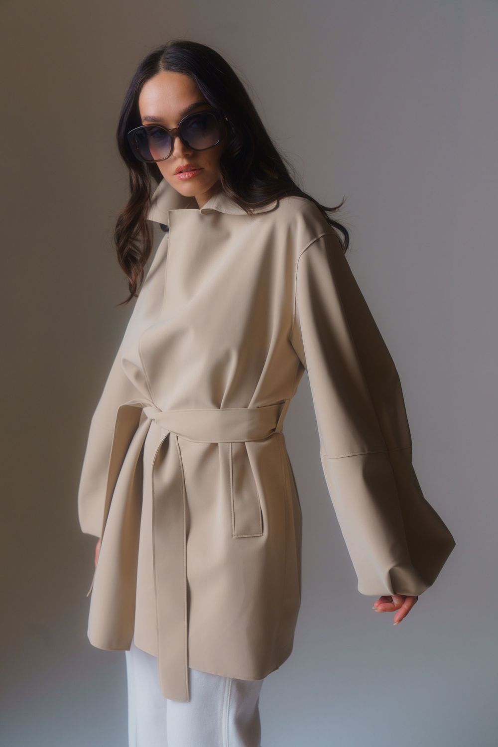 Sophisticated beige trench coat with tie waist and oversized sleeves styled with sunglasses.