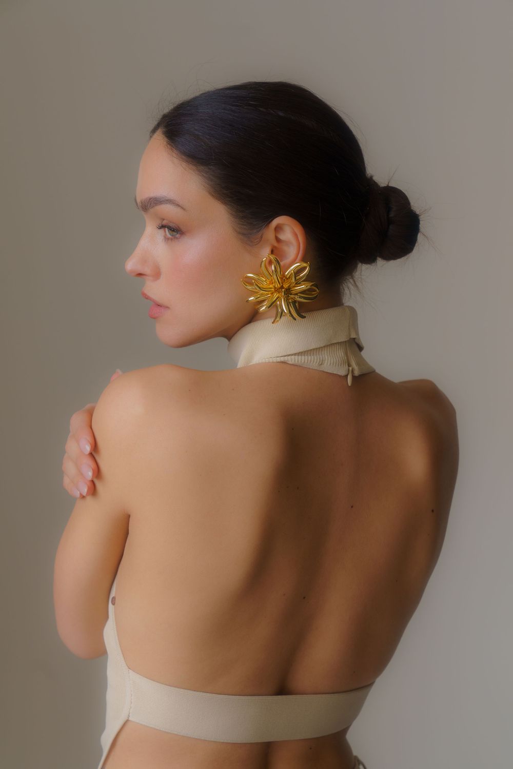 Elegant fashion photo showcasing a stunning gold statement earring and bare shoulders against neutral background.