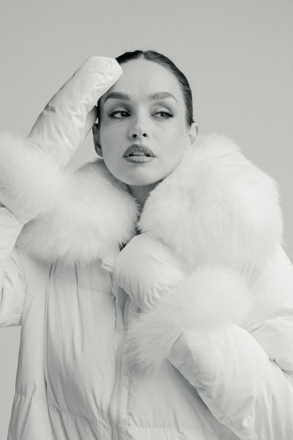 Fashion portrait in white puffy winter coat with fur trim against gray background.