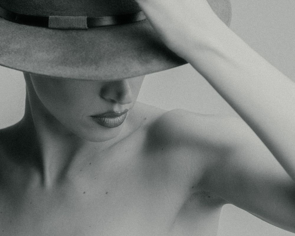Artistic black and white portrait showing a figure in a hat with shadow creating a mysterious elegant mood.