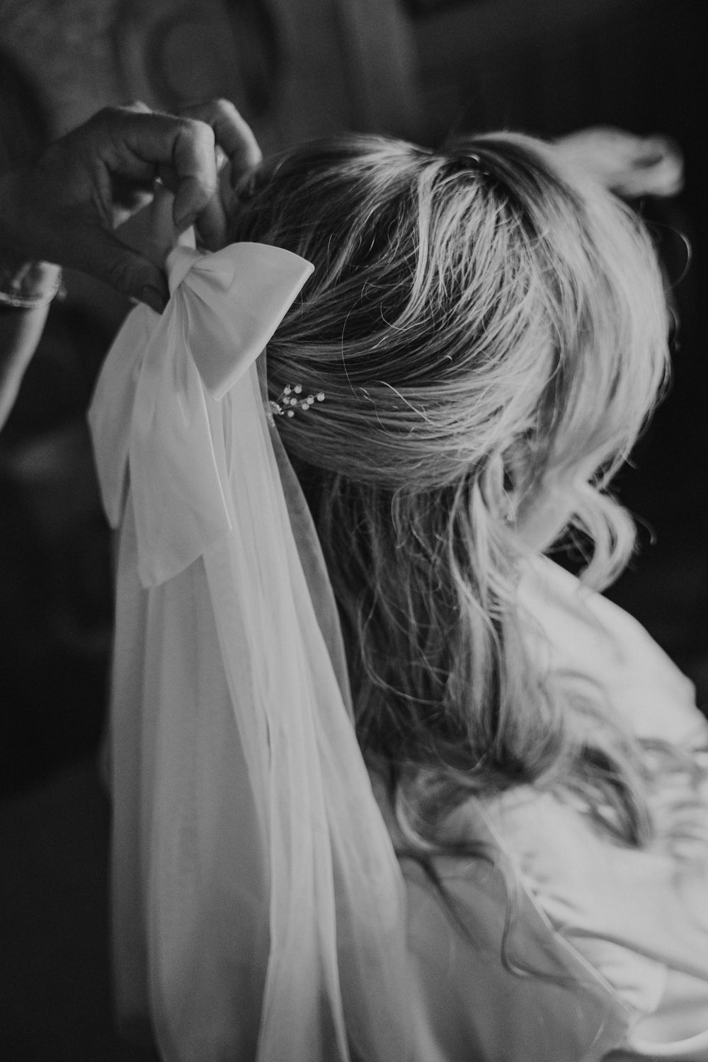 Black and white artistic photo showing delicate veil fabric being lifted with flowing blonde hair in soft motion.