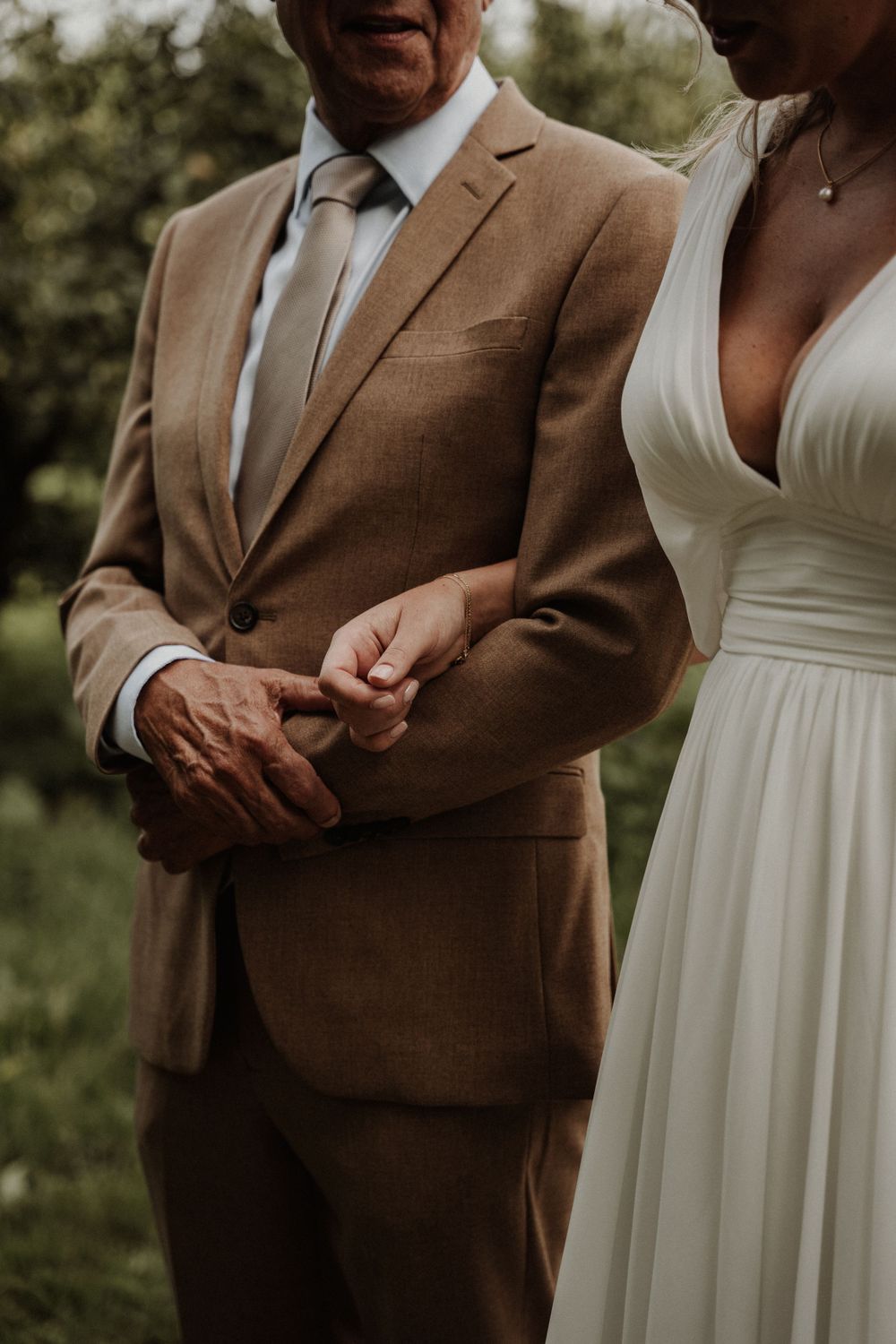 Close-up detail of wedding attire showing a brown suit jacket next to a white v-neck bridal gown in an outdoor setting.