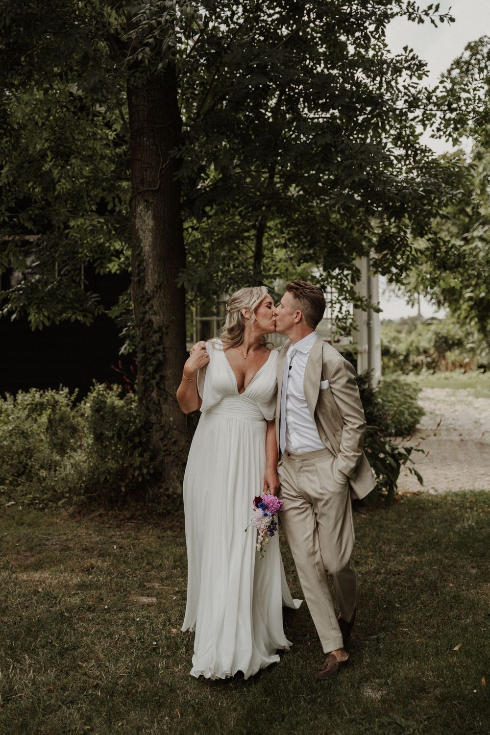 A romantic wedding couple shares an intimate moment outdoors, with the bride in a flowing white dress and groom in tan suit.