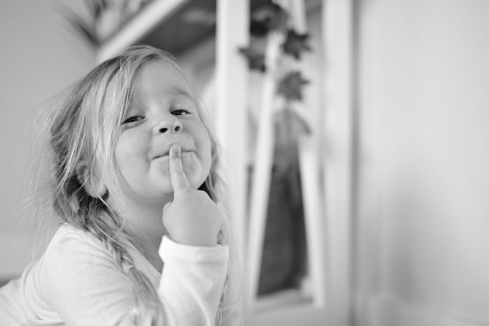 Black and white portrait of a playful child with finger on lips making a quiet gesture.