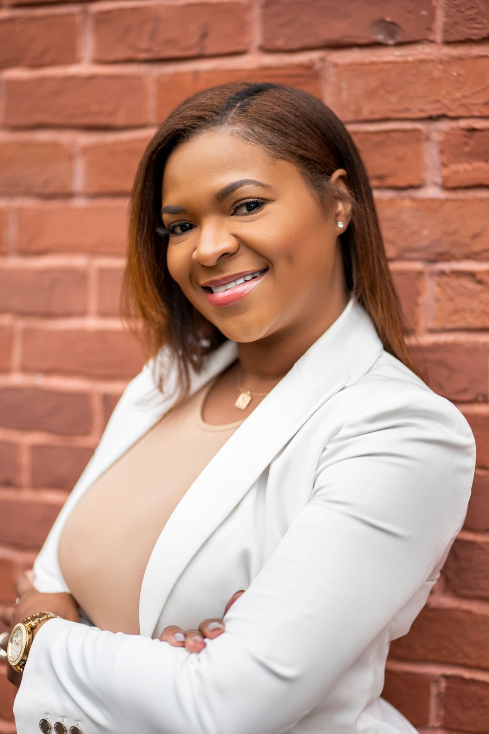 Professional in white blazer and neutral top smiling against brick wall backdrop.
