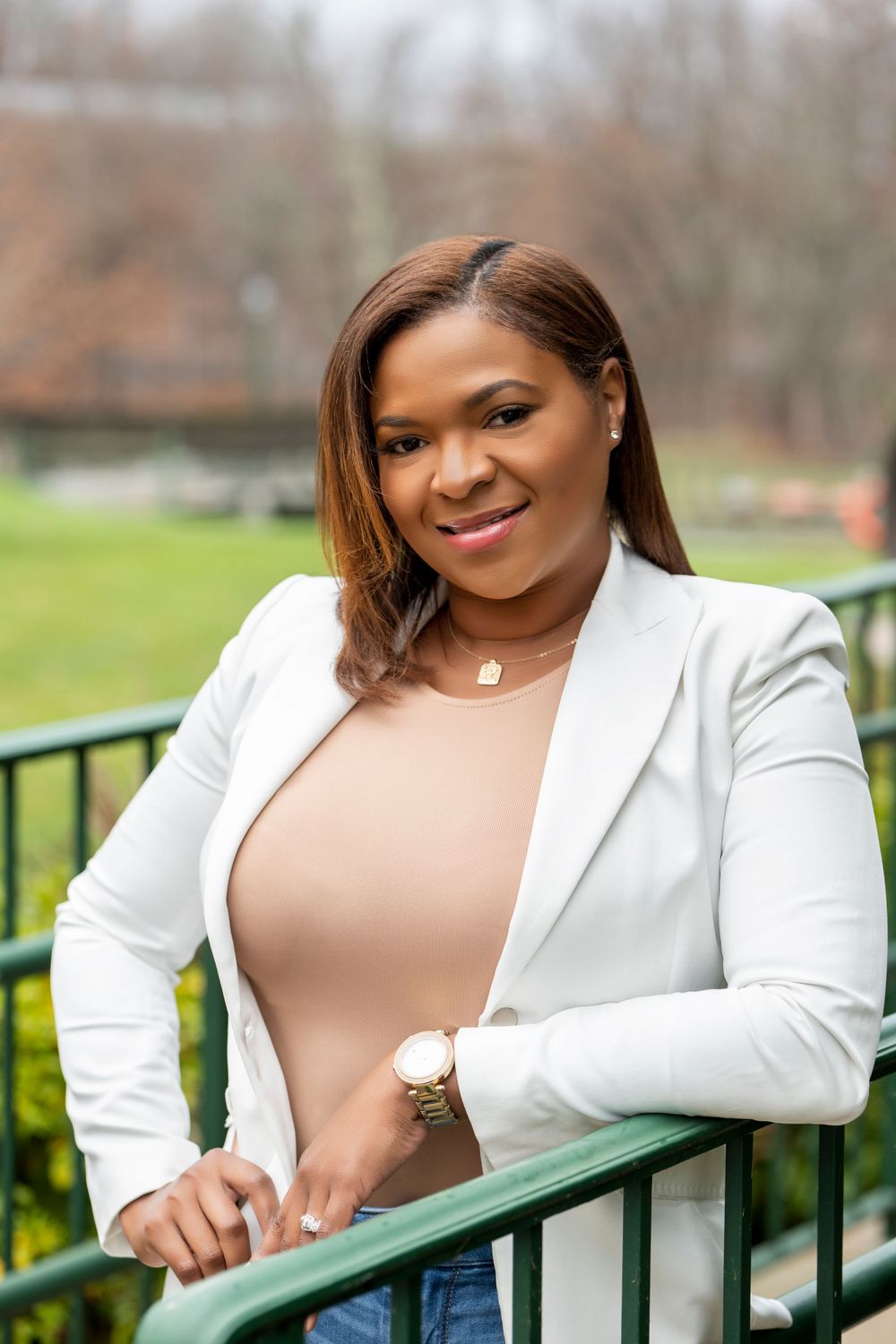 Business professional in white blazer and nude top leaning on outdoor railing.