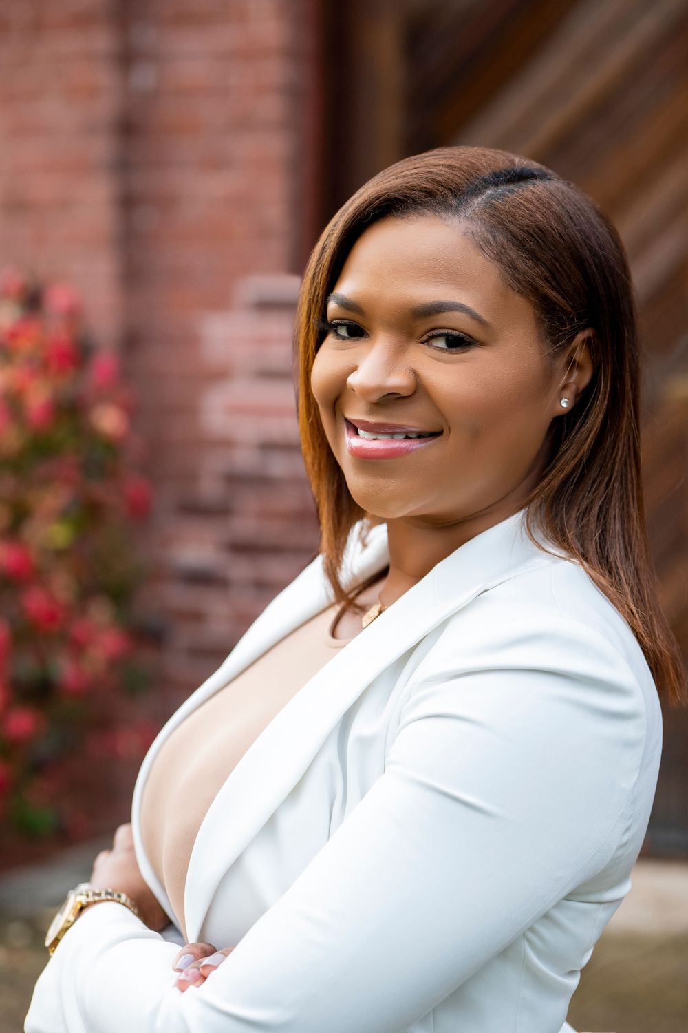 Business professional in a crisp white jacket poses confidently with decorative red flowers in background.