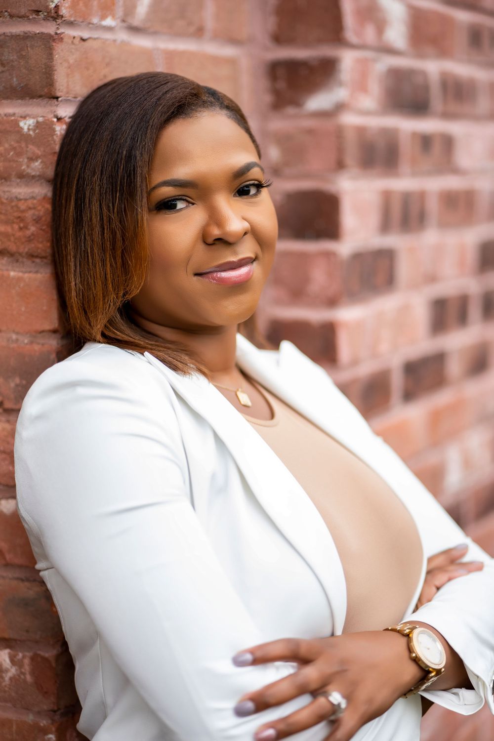 Professional headshot against brick wall featuring a white blazer and sophisticated styling.
