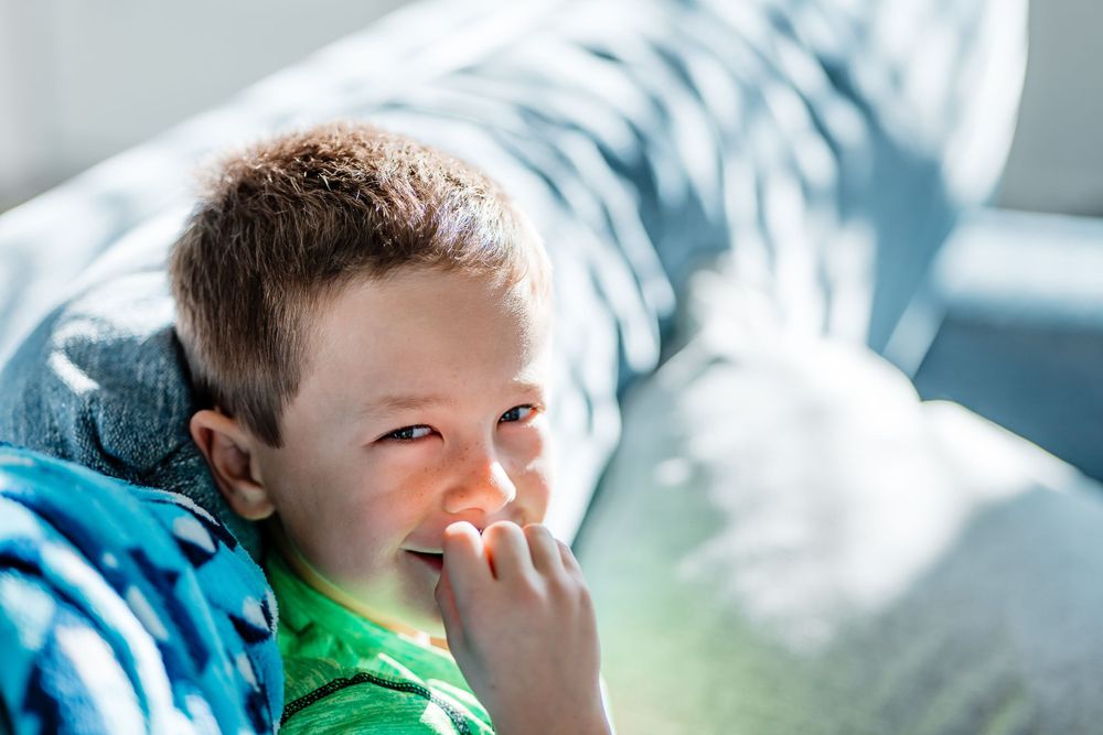 Young child in green shirt giggling while relaxing on blue couch in natural light.