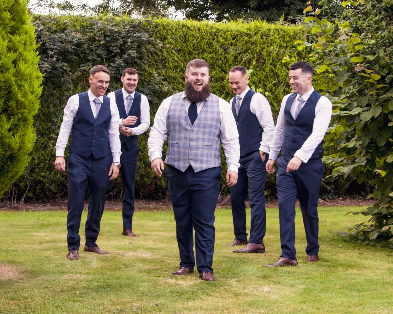Wedding party members standing in a garden setting wearing formal attire.