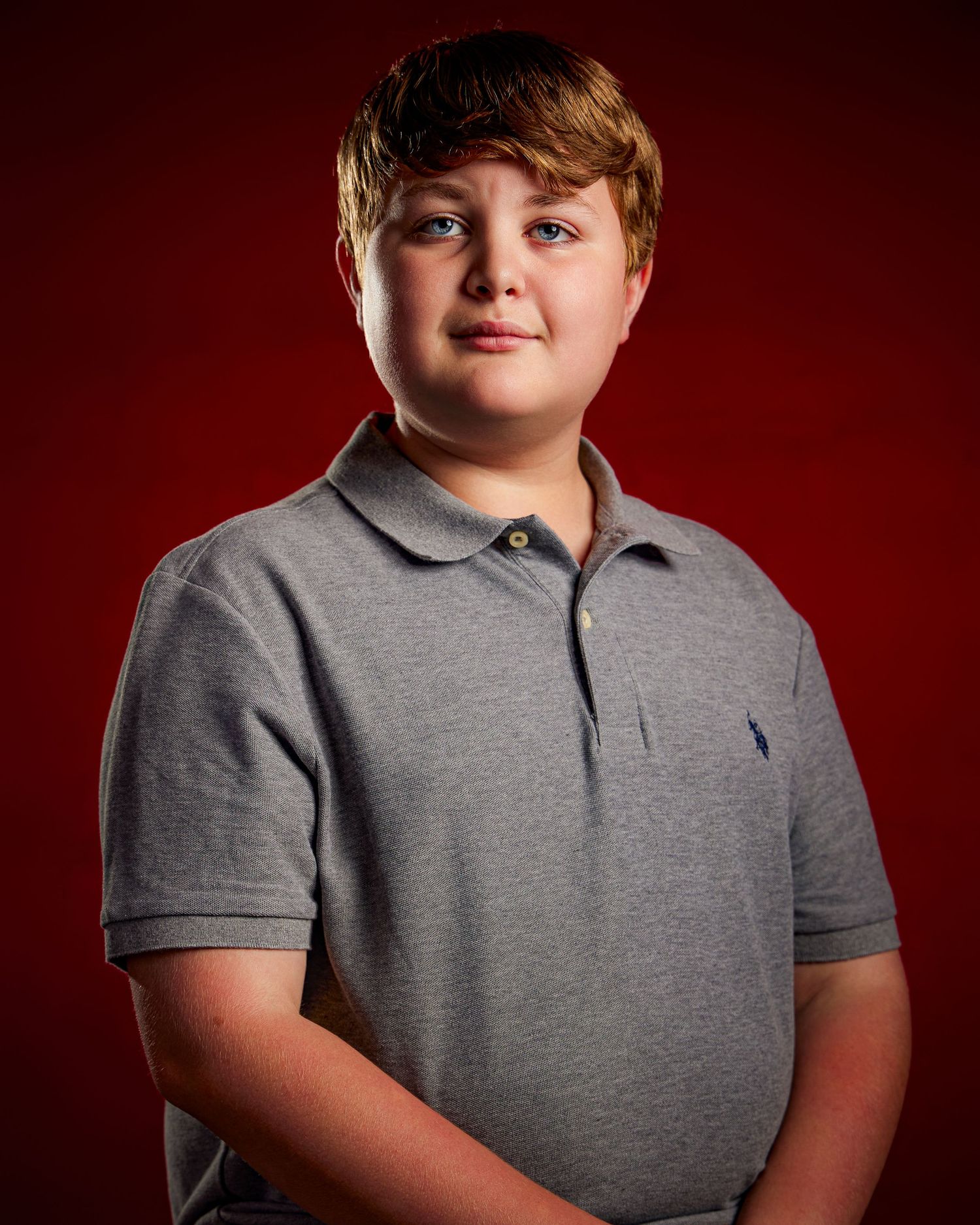 Portrait of a youth in a grey polo shirt against a burgundy background.