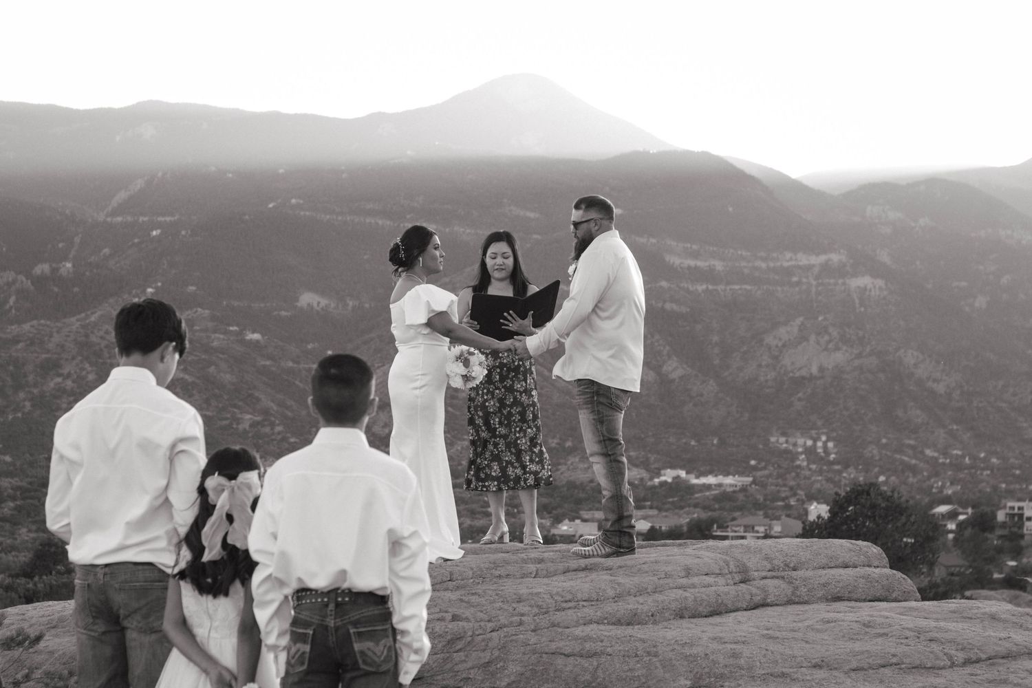 A small wedding ceremony takes place on a red rock overlook with pike peaks mountain vistas in the background in Colorado. Elopement photo