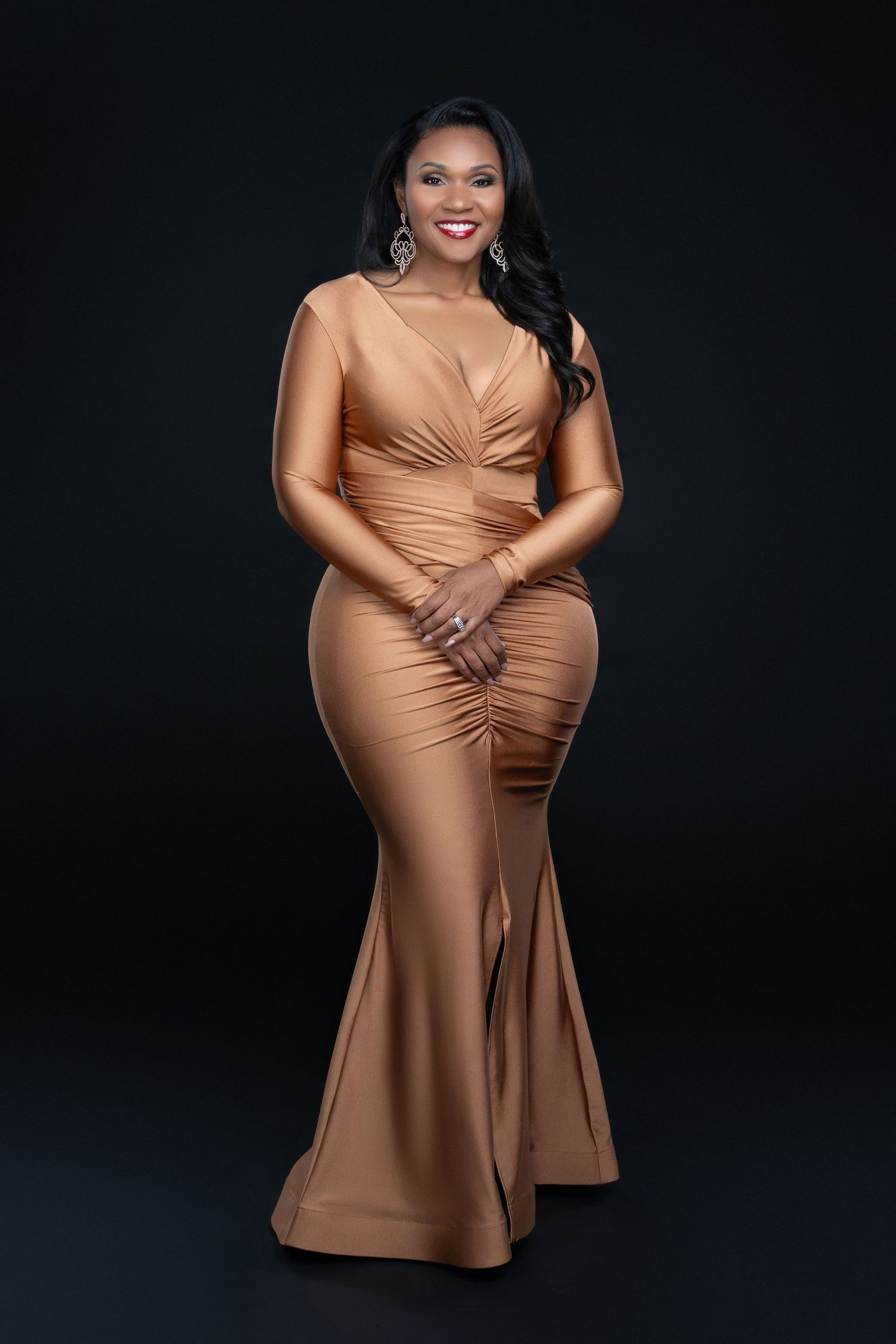 Elegant full-length photo of woman in fitted champagne-colored evening gown against dark background.