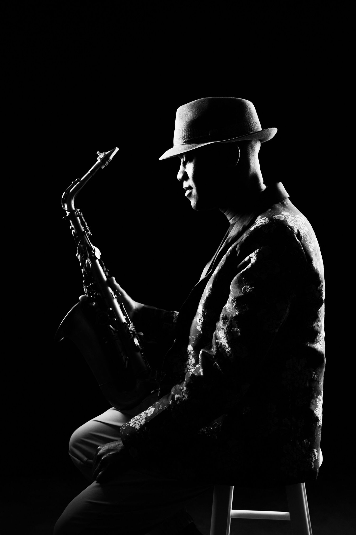 Dramatic black and white silhouette of saxophone player wearing fedora hat.