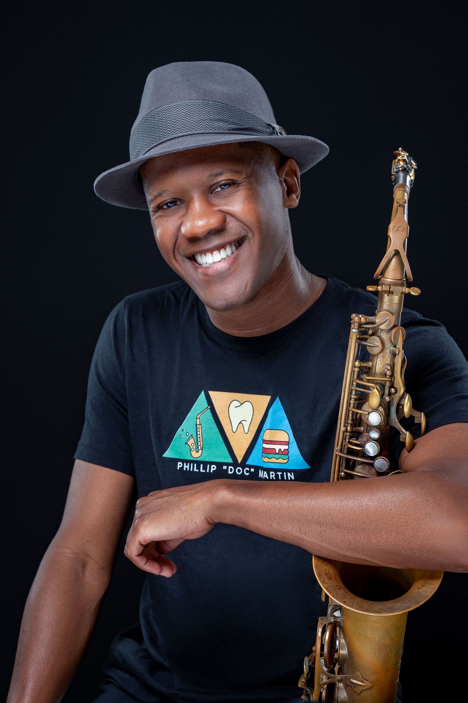 Professional studio portraits showing musician in black t-shirt holding saxophone against dark background.
