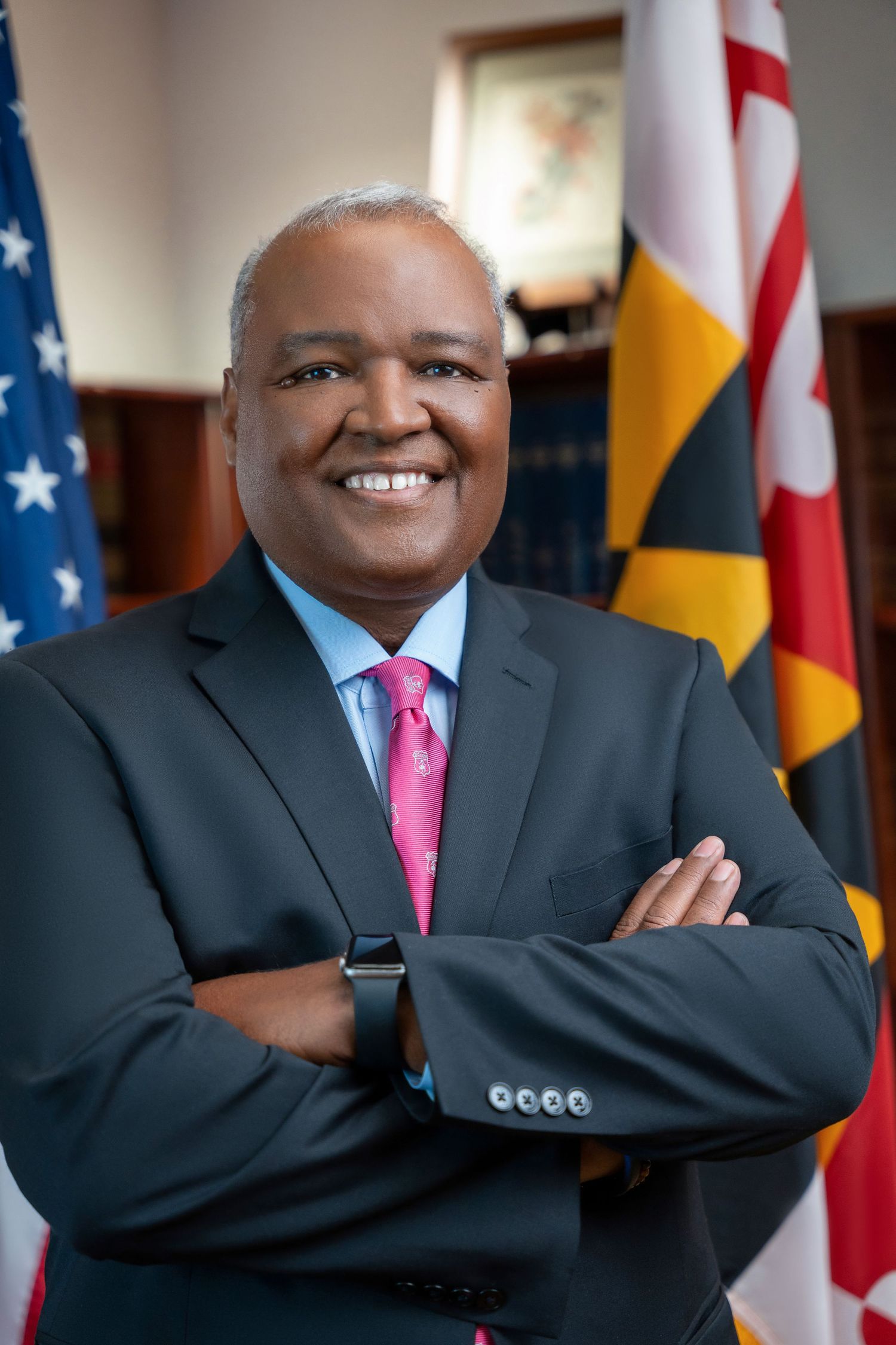 Professional portraits with American flags showing confident poses in dark suit and pink tie.