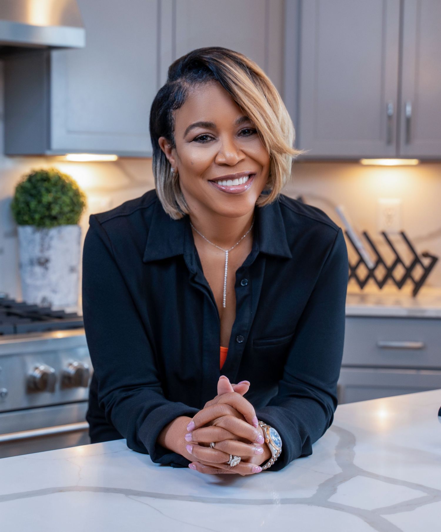 Professional headshot of someone in a black shirt leaning on a white kitchen counter with warm lighting.