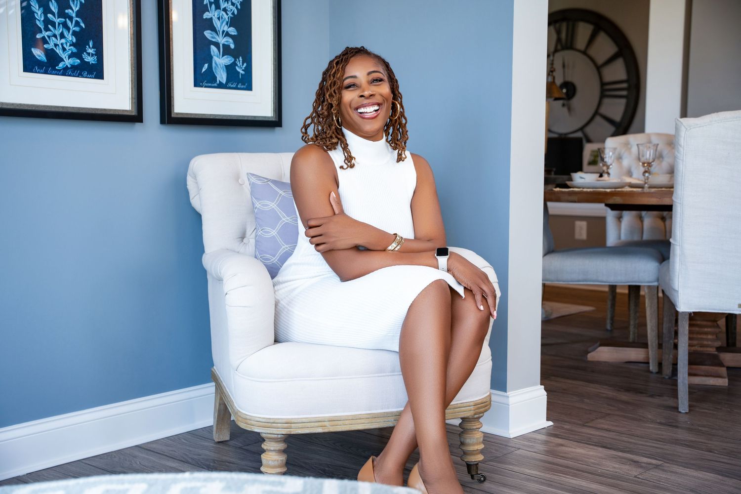 Elegant portrait of someone in white sleeveless dress seated in a plush white armchair.