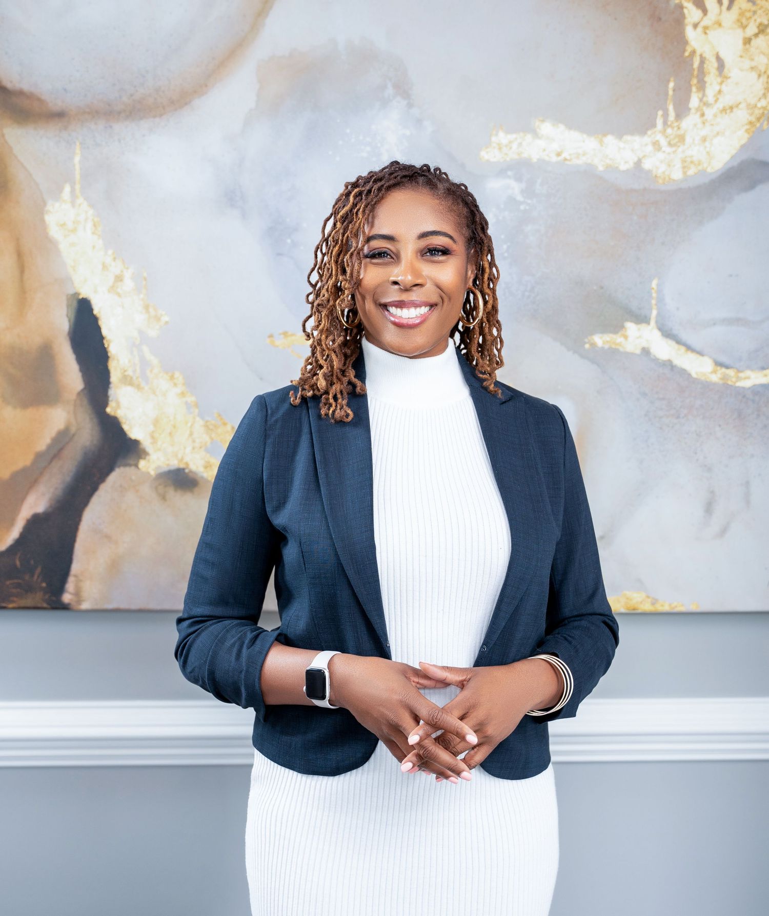 Professional portrait with white turtleneck and navy blazer against marble and gold abstract background.