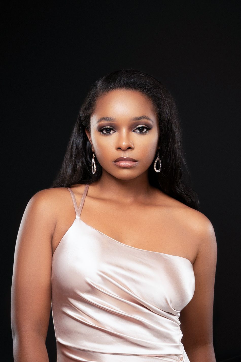Glamour portrait in ivory satin one-shoulder dress against dark background with silver earrings.