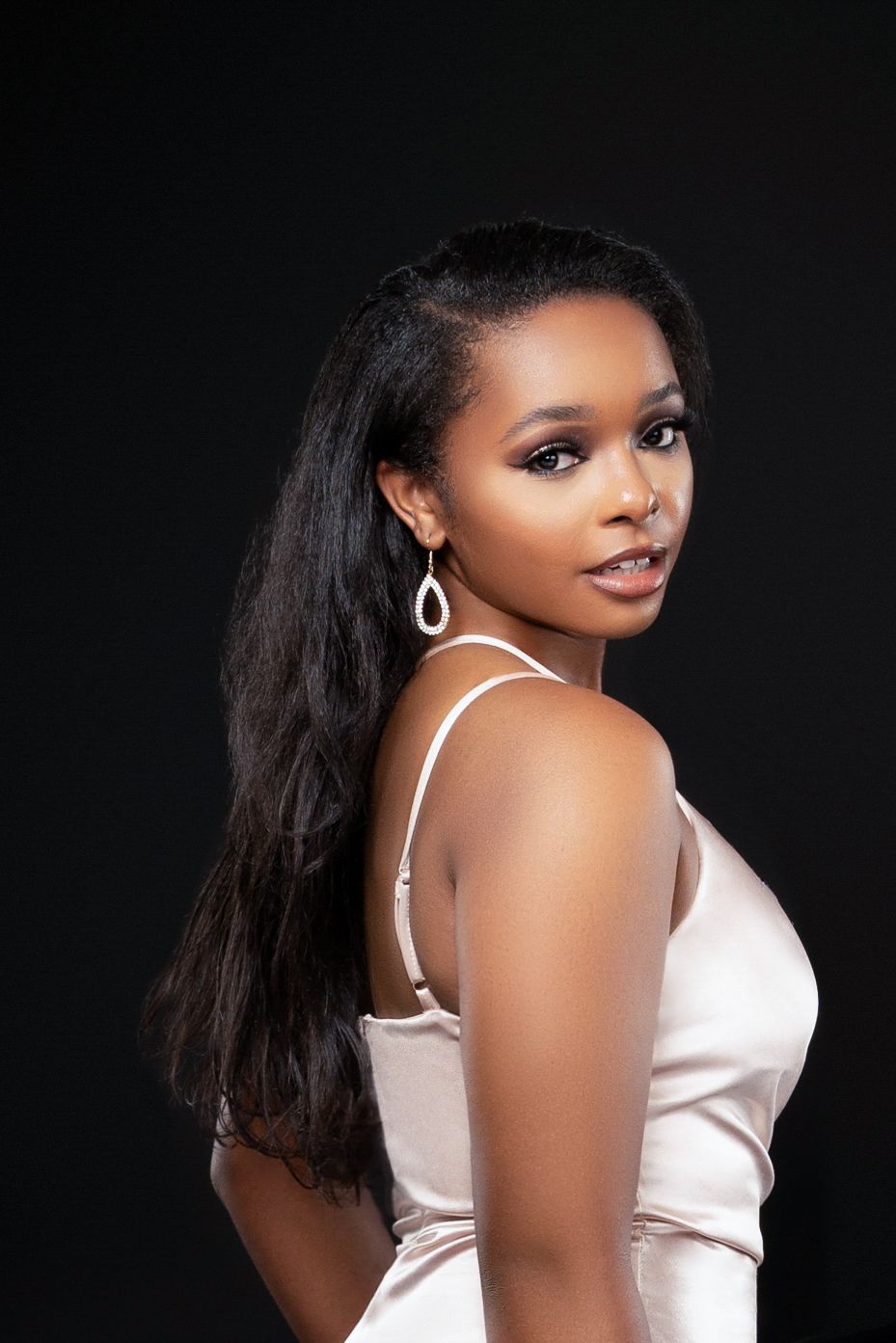 Elegant side profile portrait in ivory satin dress with long dark hair and statement earrings.