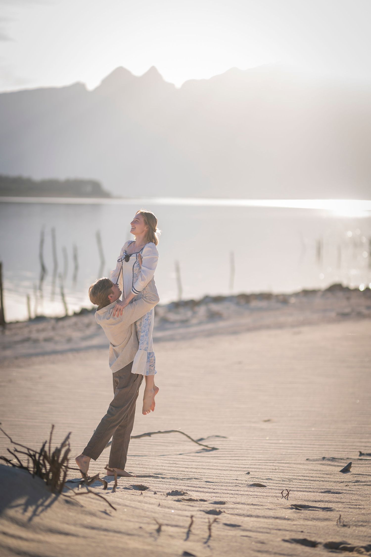 Parent and child play together at sunset on a misty beach with driftwood and mountains in the background.