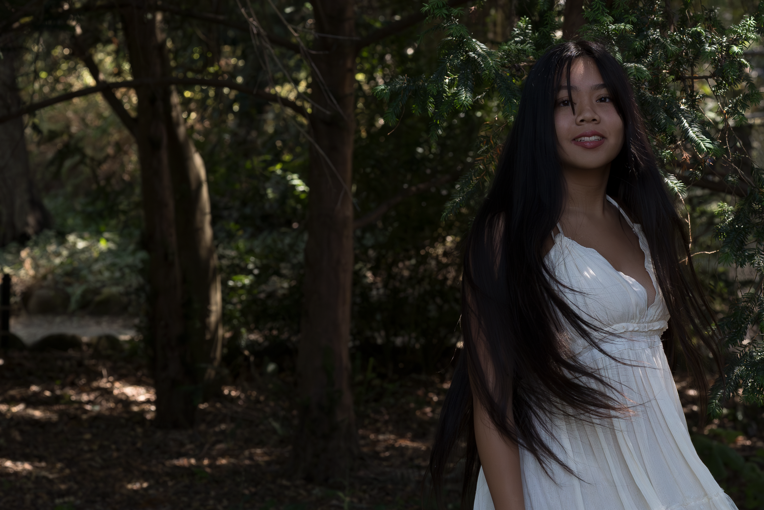 A white dress moves gracefully among trees in a natural outdoor setting.