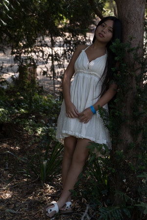 A white summer dress flows in the dappled sunlight of a wooded garden setting.