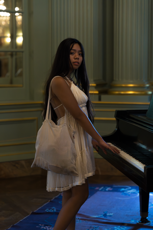 A white flowy dress catches light while someone performs at a grand piano indoors.