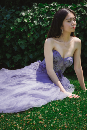 Figure in lavender tulle gown reclining on grass in garden setting.