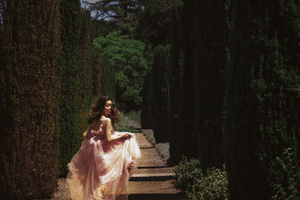 Figure in pink dress walking through sunlit forest path.