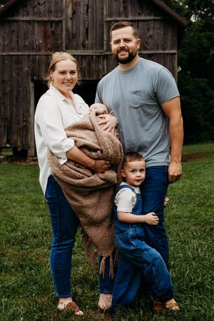 A casual family photo session shows casual outfits and warm embraces against a rustic barn backdrop.