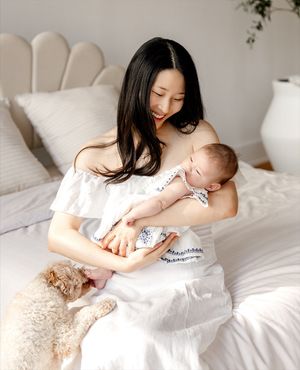 Parent and infant sharing tender moments together on white bedding in natural morning light.